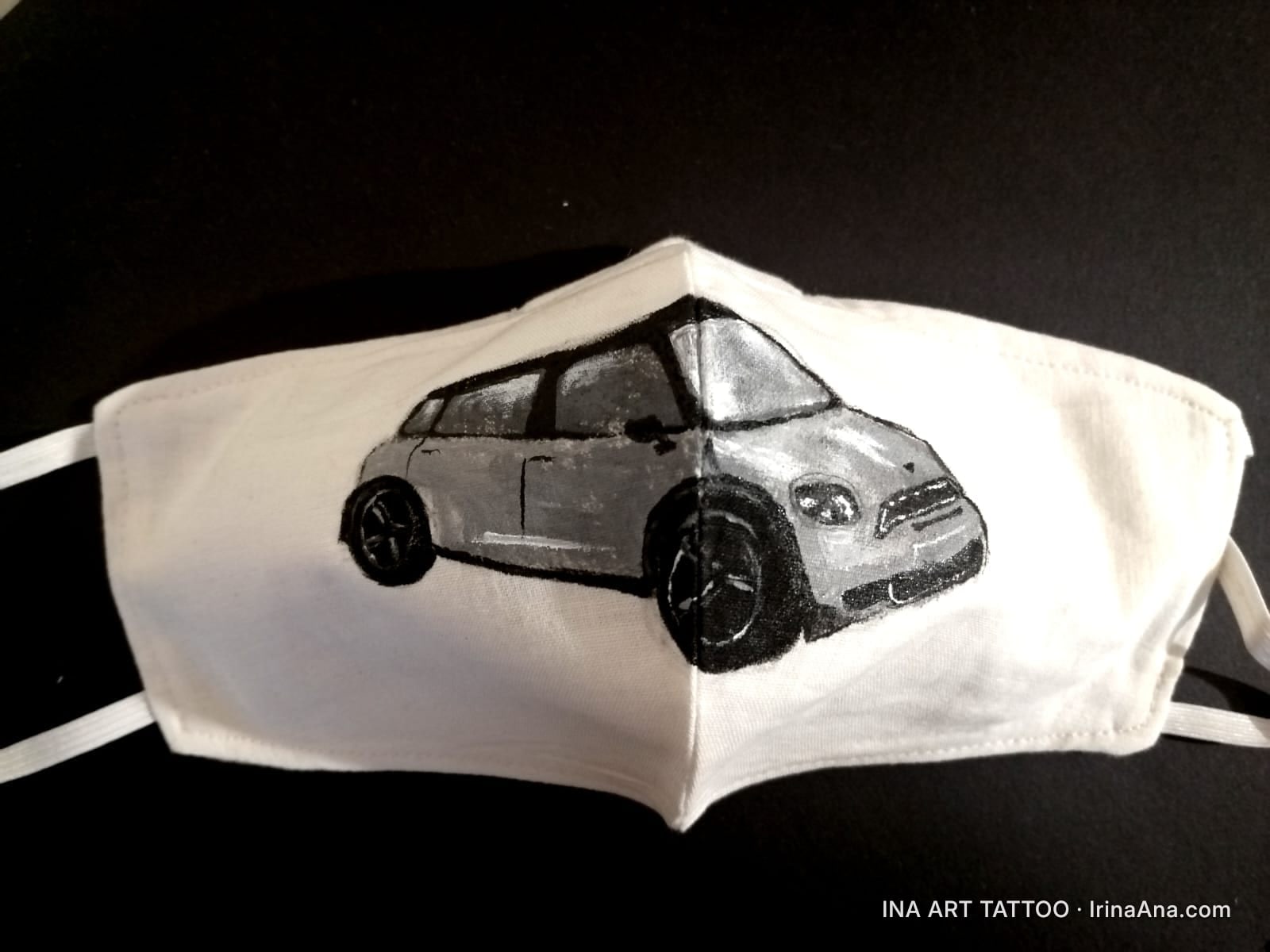 O mască de față albă din pânză, cu o pictură în acrilic a unei mașini Mini Cooper gri pe partea din față.