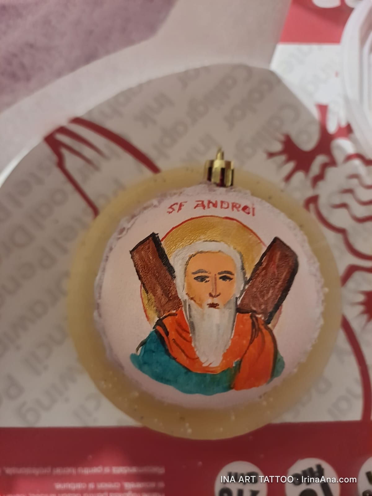 Un glob de Crăciun cu o pictură stilizată a Sfântului Andrei, având o barbă albă și o aură aurie, ținând o cruce.