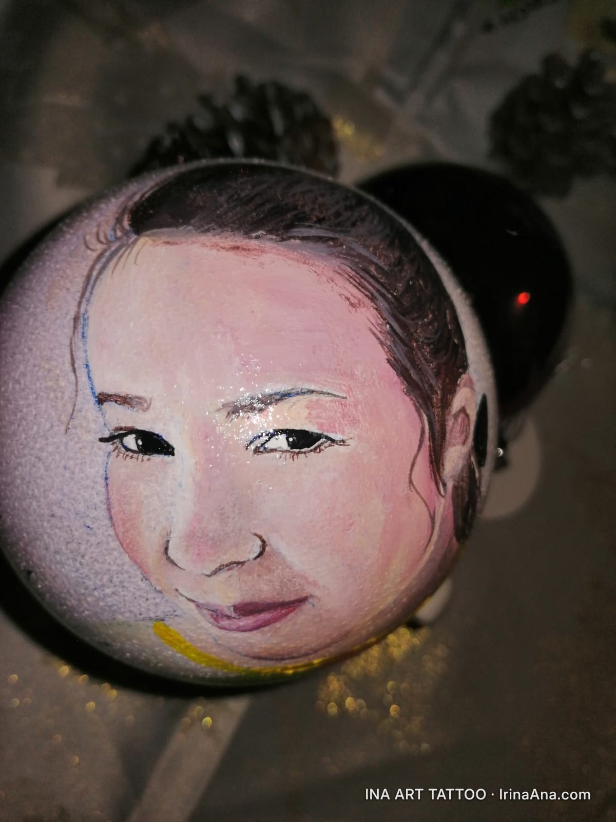 Un ornament de Crăciun rotund, pictat manual, cu un portret detaliat al unei femei asiatice, zâmbind ușor.