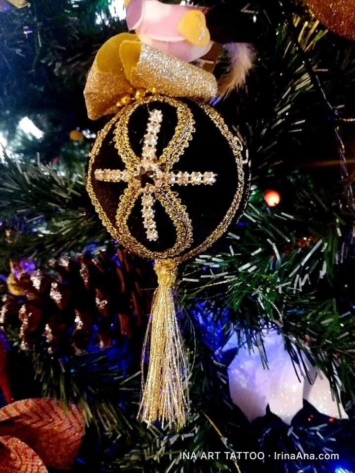 Un ornament de Crăciun negru, decorat cu sclipici auriu și pietre albe, atârnând într-un brad. Are un ciucure auriu.