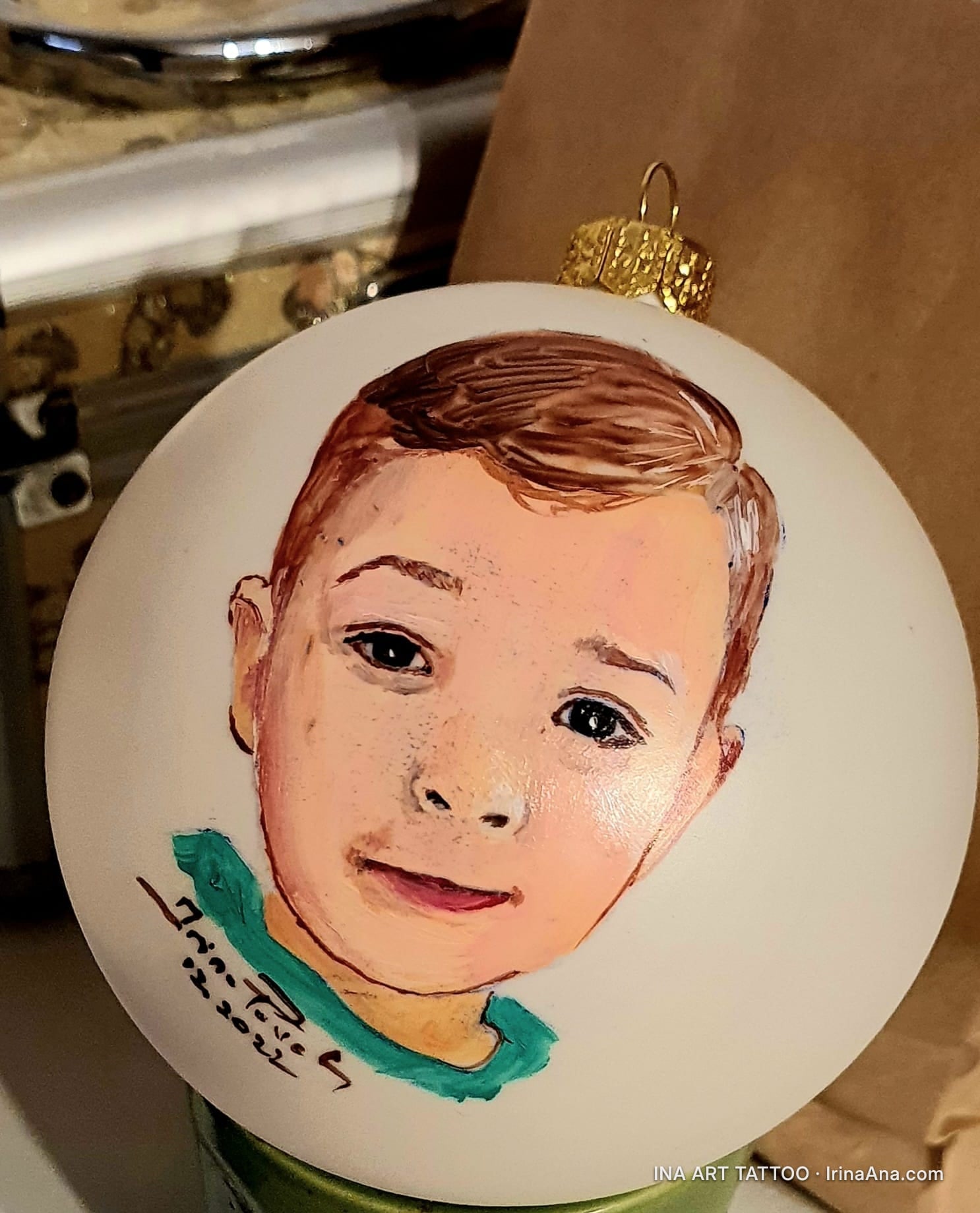 Un ornament alb de Crăciun, pictat manual cu portretul unui copil cu păr șaten și pistrui, zâmbind ușor.