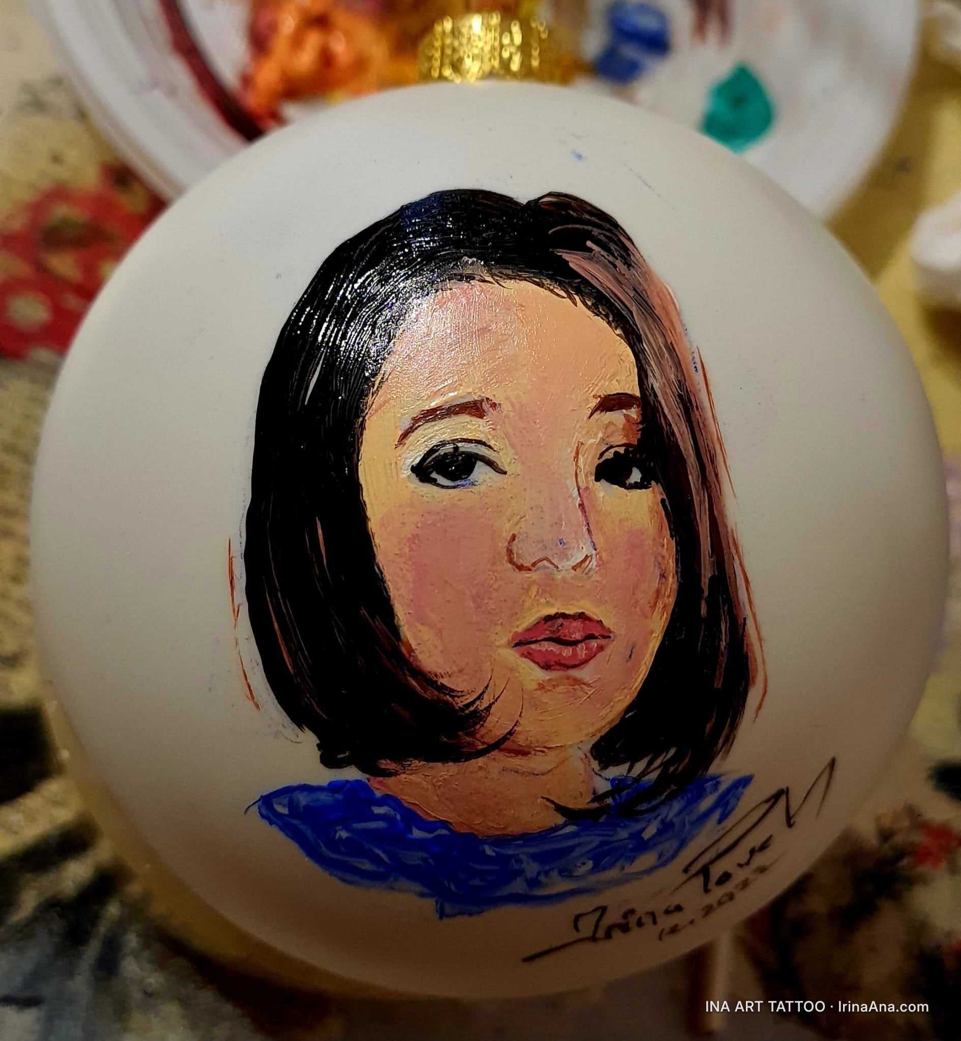 Un portret de femeie cu păr scurt, în nuanțe calde, pictat pe un glob de Crăciun alb.
