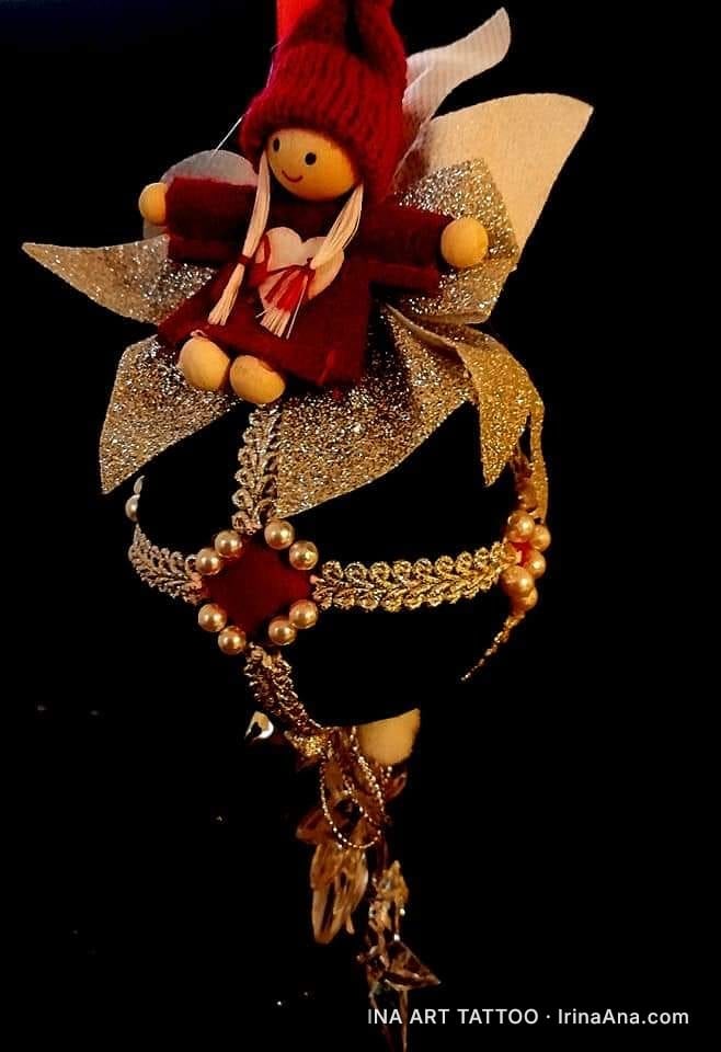 Un ornament de Crăciun cu un spiriduș, o fundă aurie și decorațiuni cu perle, pe un fundal negru.