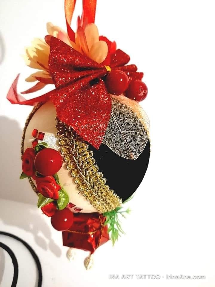 Un ornament de Crăciun artizanal, decorat cu o fundă roșie sclipitoare, flori, frunze scheletice și bobițe roșii.