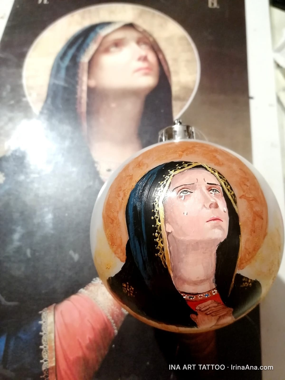Un glob de Crăciun pictat manual, înfățișând o icoană religioasă cu o femeie în rugăciune, cu lacrimi pe față.