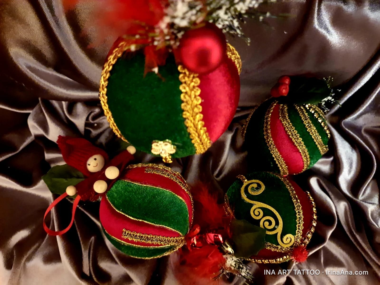 Patru ornamente de Crăciun lucrate manual, în nuanțe de roșu și verde, decorate cu panglici aurii, așezate pe un material sa…