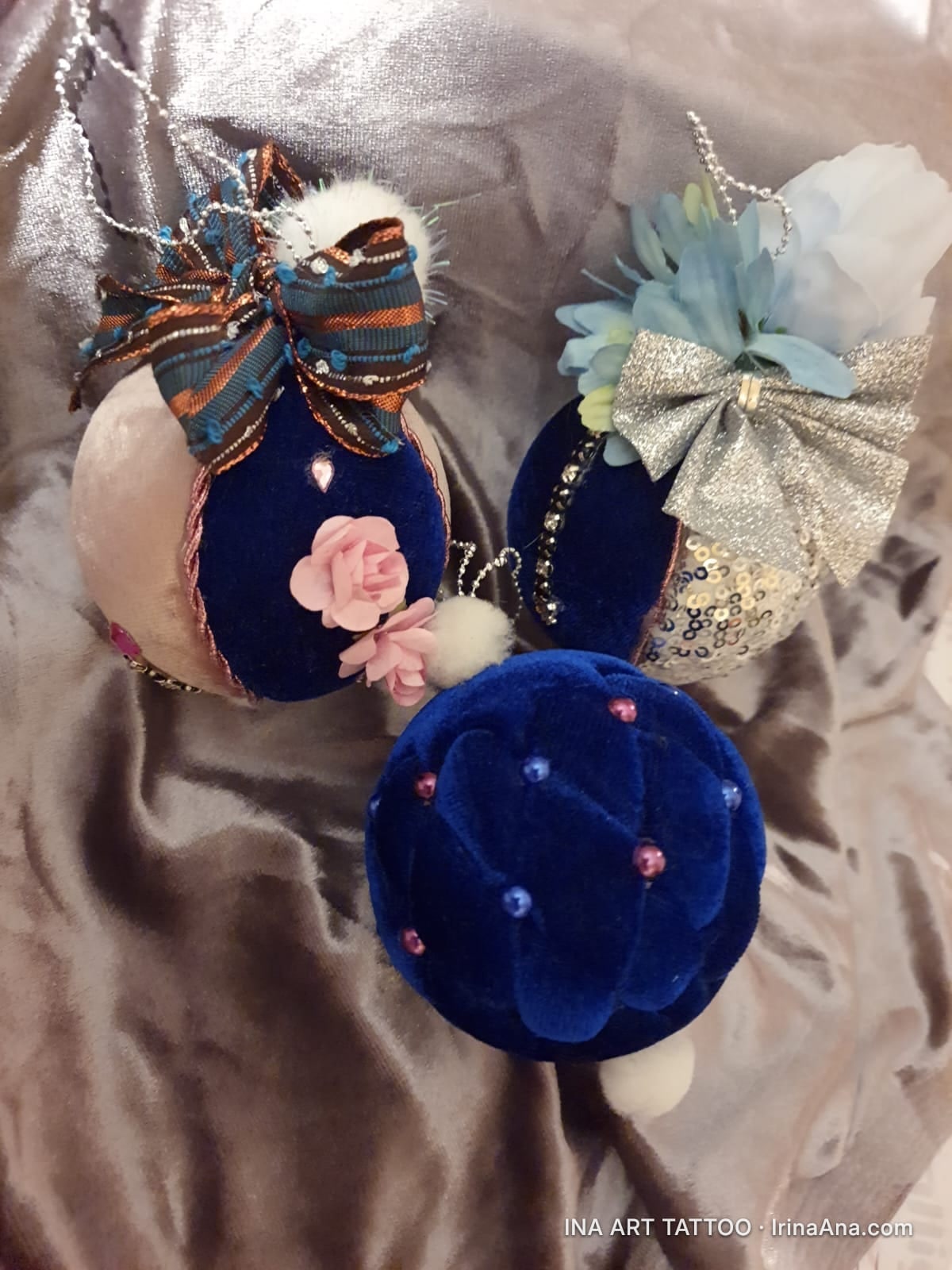 Trei ornamente de Crăciun lucrate manual, decorate cu panglici, paiete și perle, așezate pe o țesătură moale.