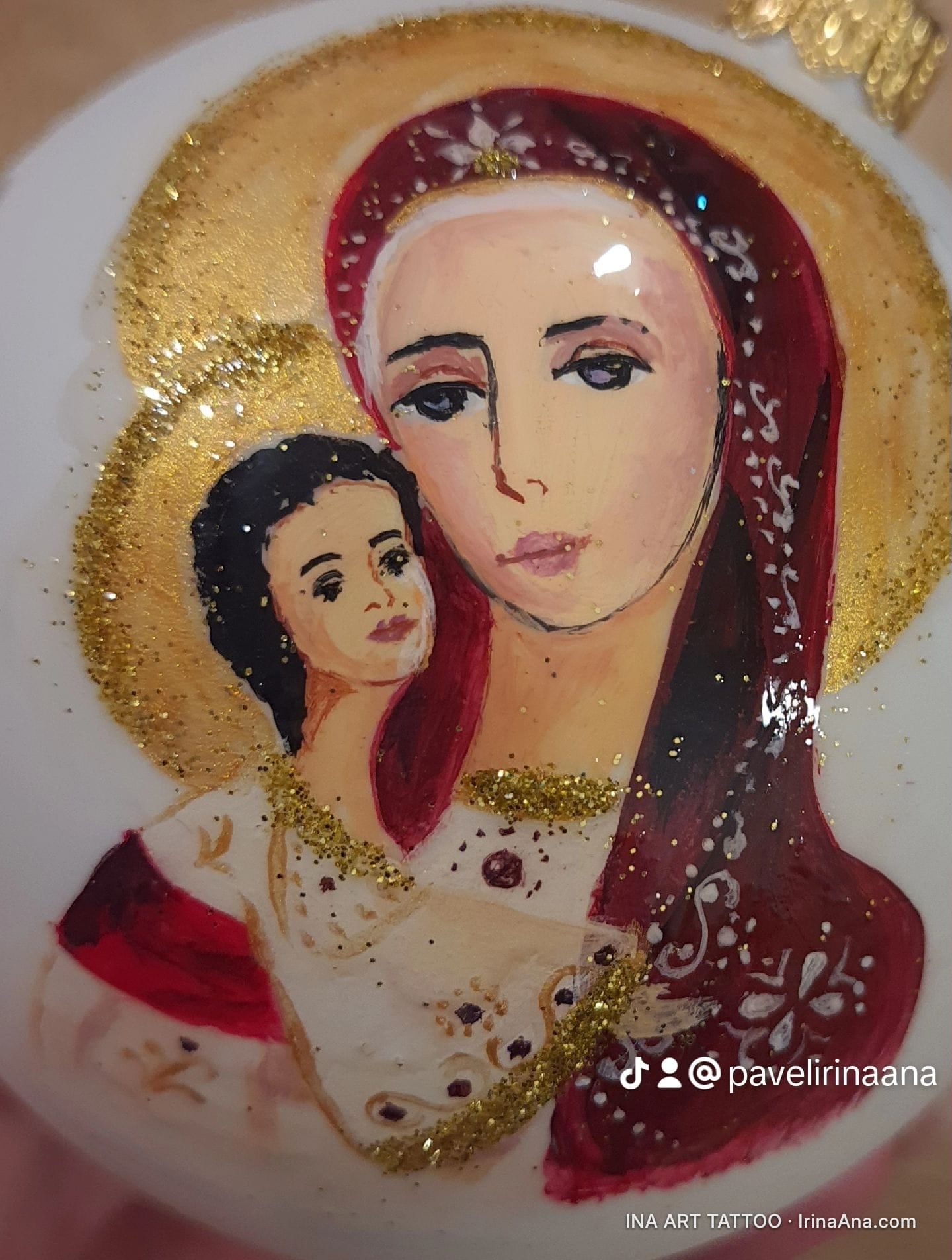 Un glob de Crăciun alb, pictat manual, înfățișând-o pe Fecioara Maria cu Pruncul Iisus, cu aure aurii și sclipici.