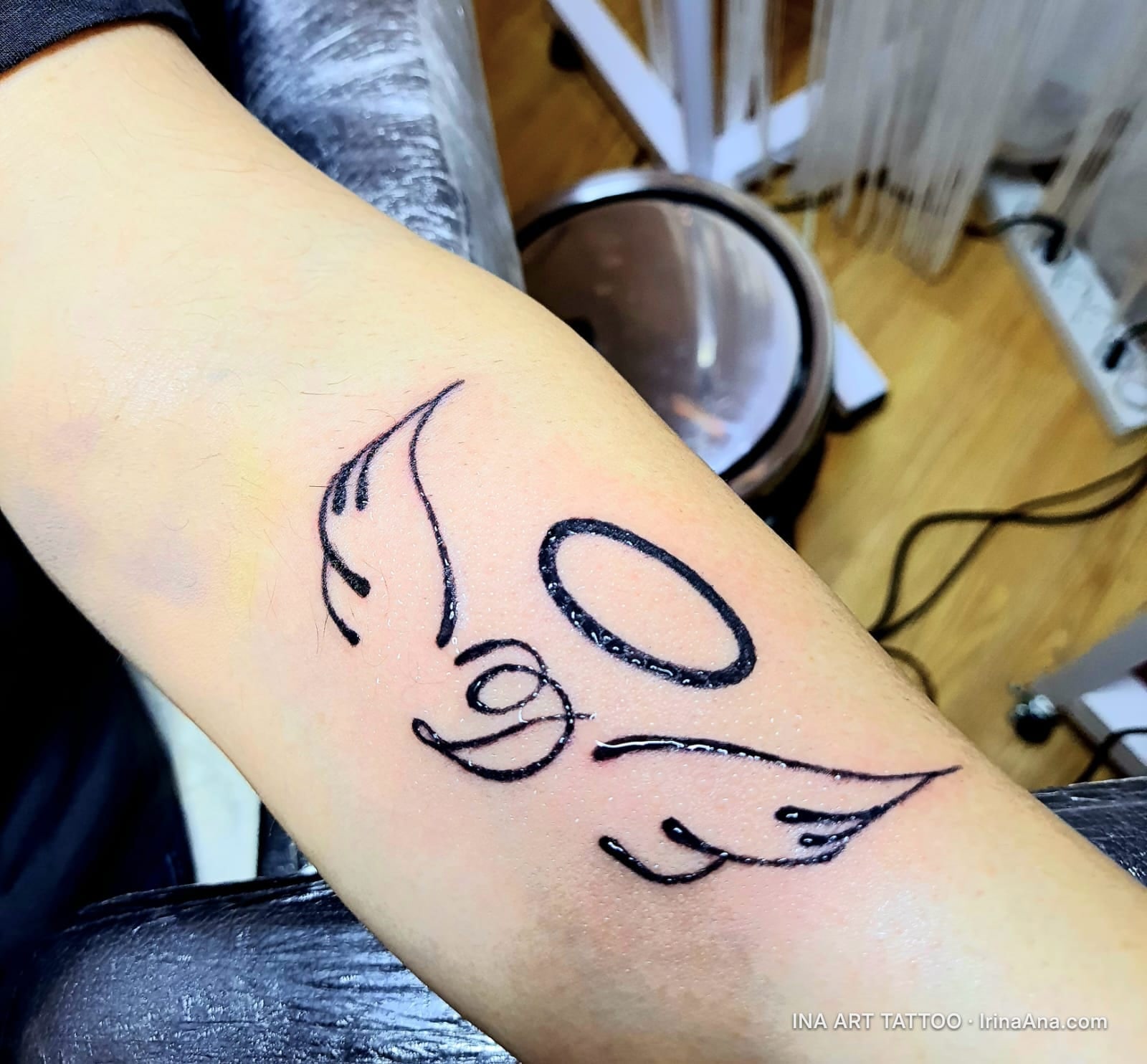Minimalist tattoo on forearm with angel wings and a halo, made with simple black lines.
