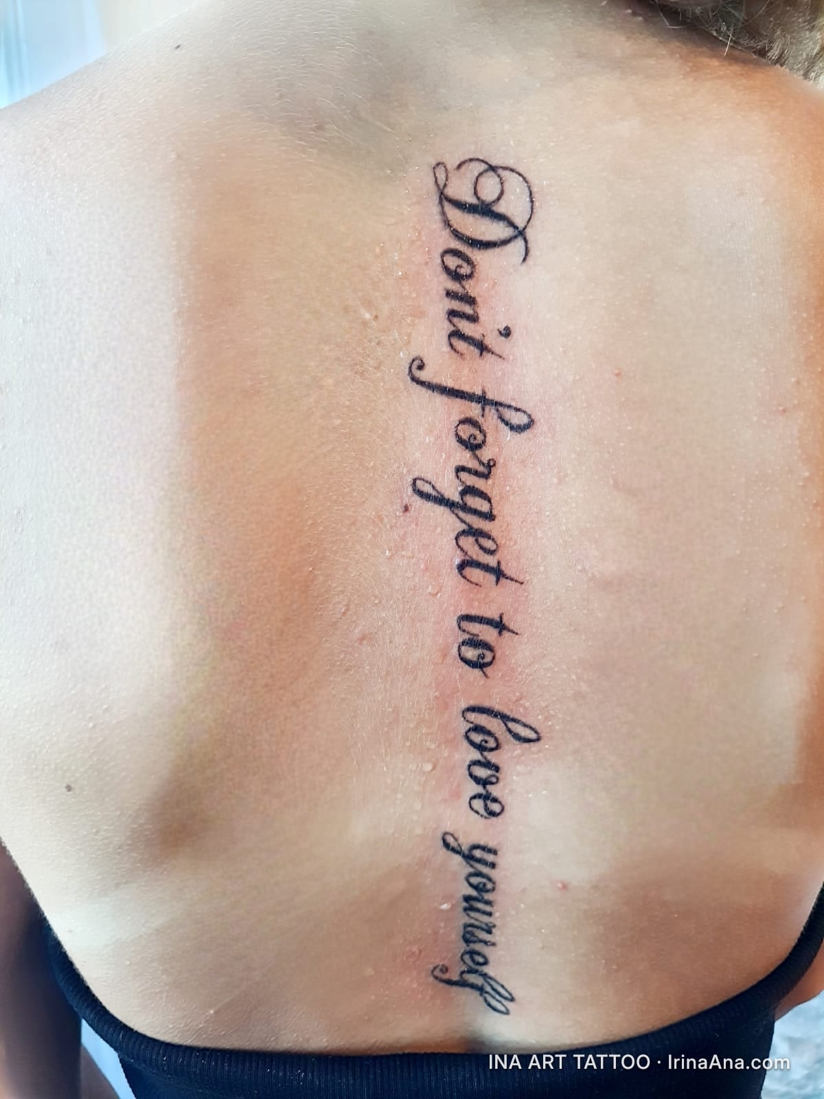 Tattoo with the text "Don't forget to love yourself" written vertically on a person's upper back.