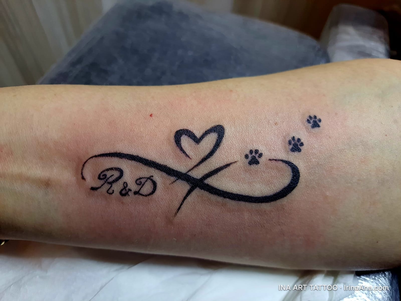 Tattoo on forearm with an infinity symbol, a heart outline, and three paw prints.