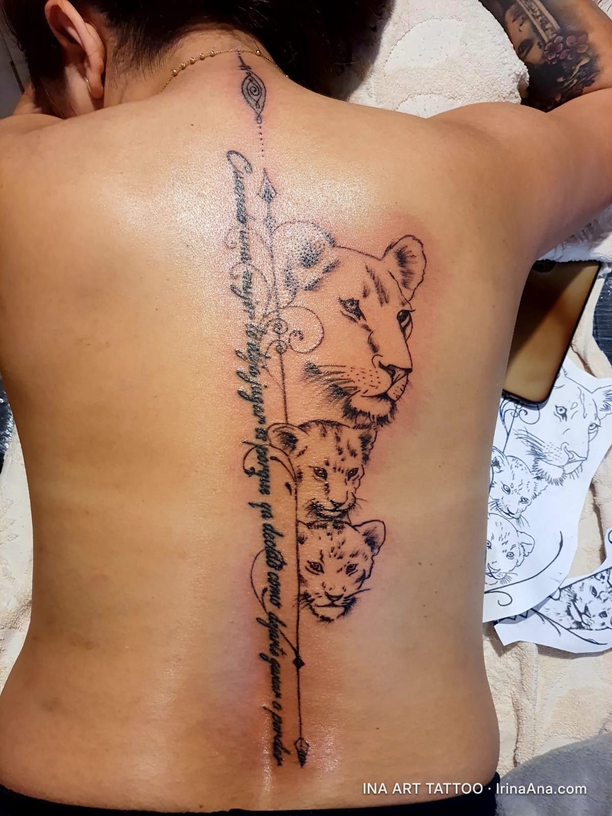Back tattoo featuring a lioness and two lion cubs, alongside calligraphic text, arranged vertically along the spine.