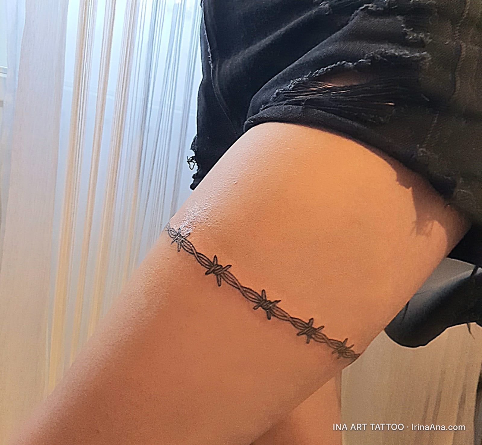 Barbed wire tattoo wrapped around a person's thigh. The wire is realistically drawn with small barbs.