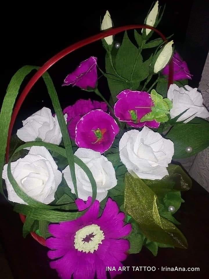 Basket with crepe paper flowers: white roses, purple flowers, and buds, with green leaves and a golden ribbon.