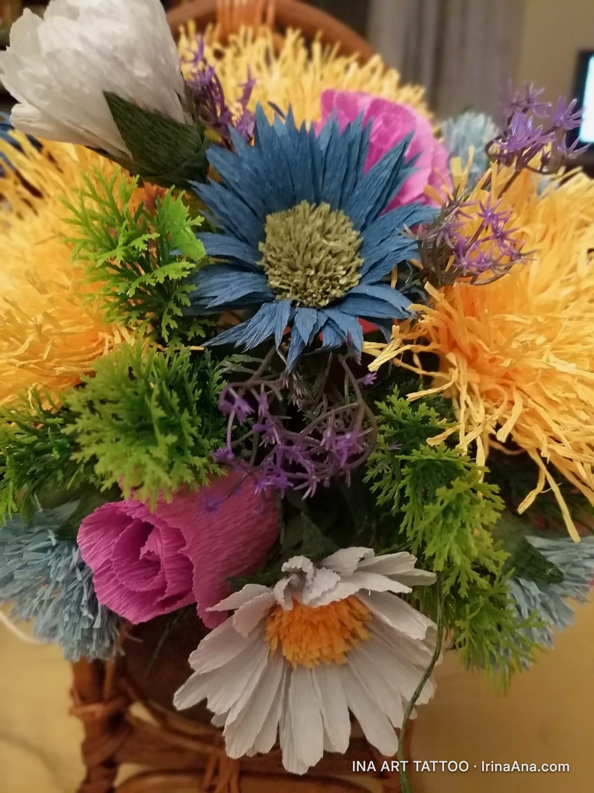 A handmade floral arrangement, featuring crepe paper flowers in shades of blue, white, pink, yellow, and green.