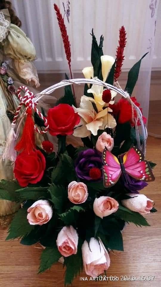A decorative basket with artificial crepe paper flowers, including roses, lilies, and a pink butterfly.