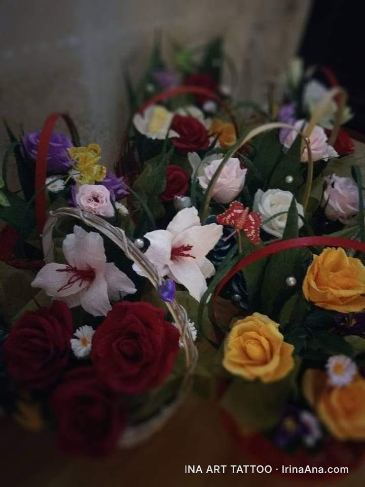 Several small baskets filled with artificial flowers made of crepe paper, in various vibrant colors, with green leaves and d…