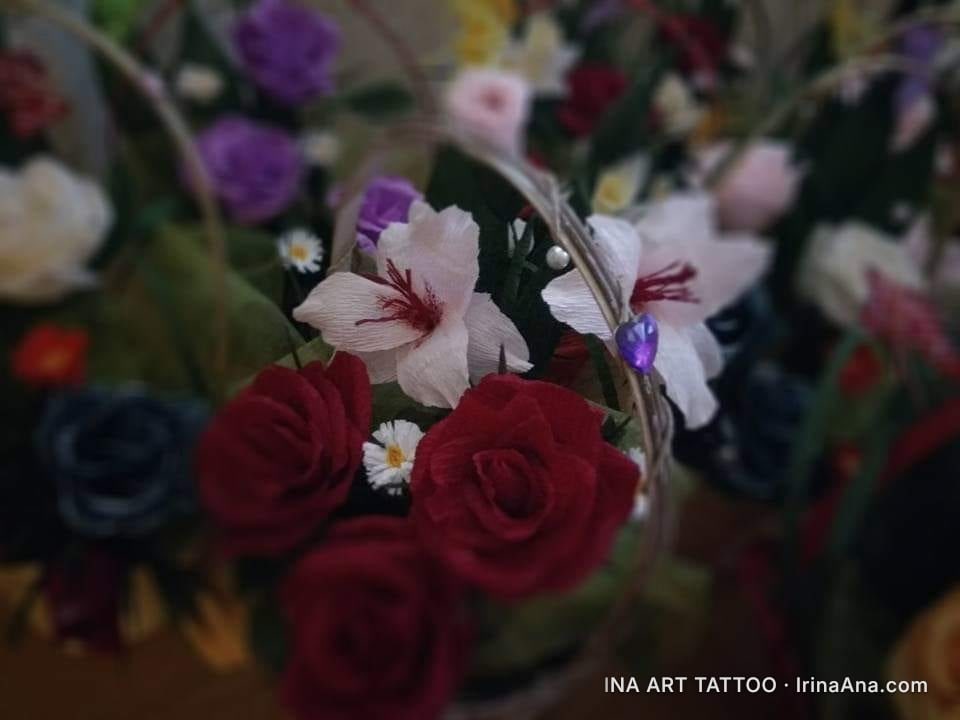 Crepe paper flower arrangement with red roses, white lilies, and daisies in a small basket.