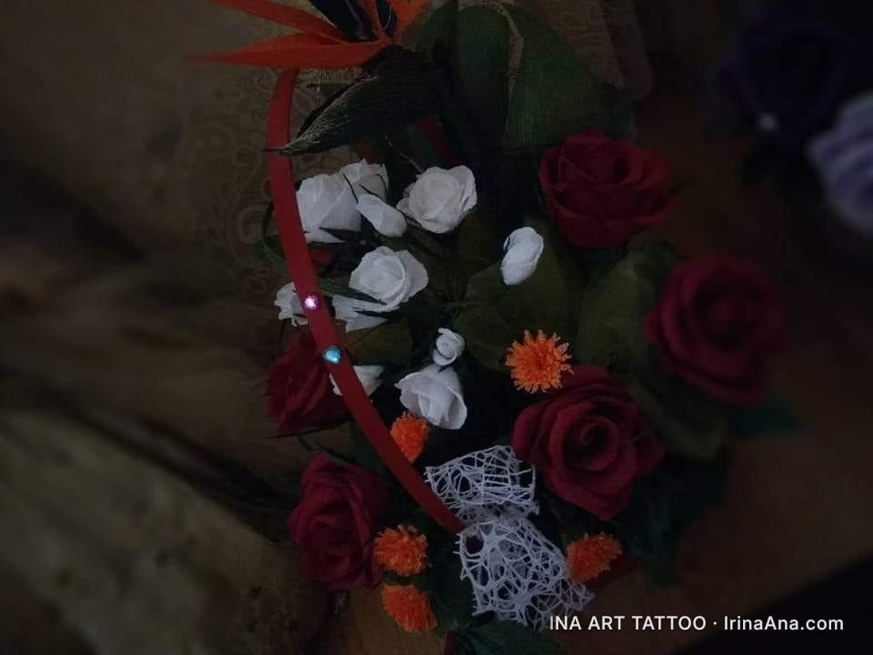 A bouquet of artificial crepe paper flowers, featuring red and white roses, orange blossoms, and a bird of paradise.