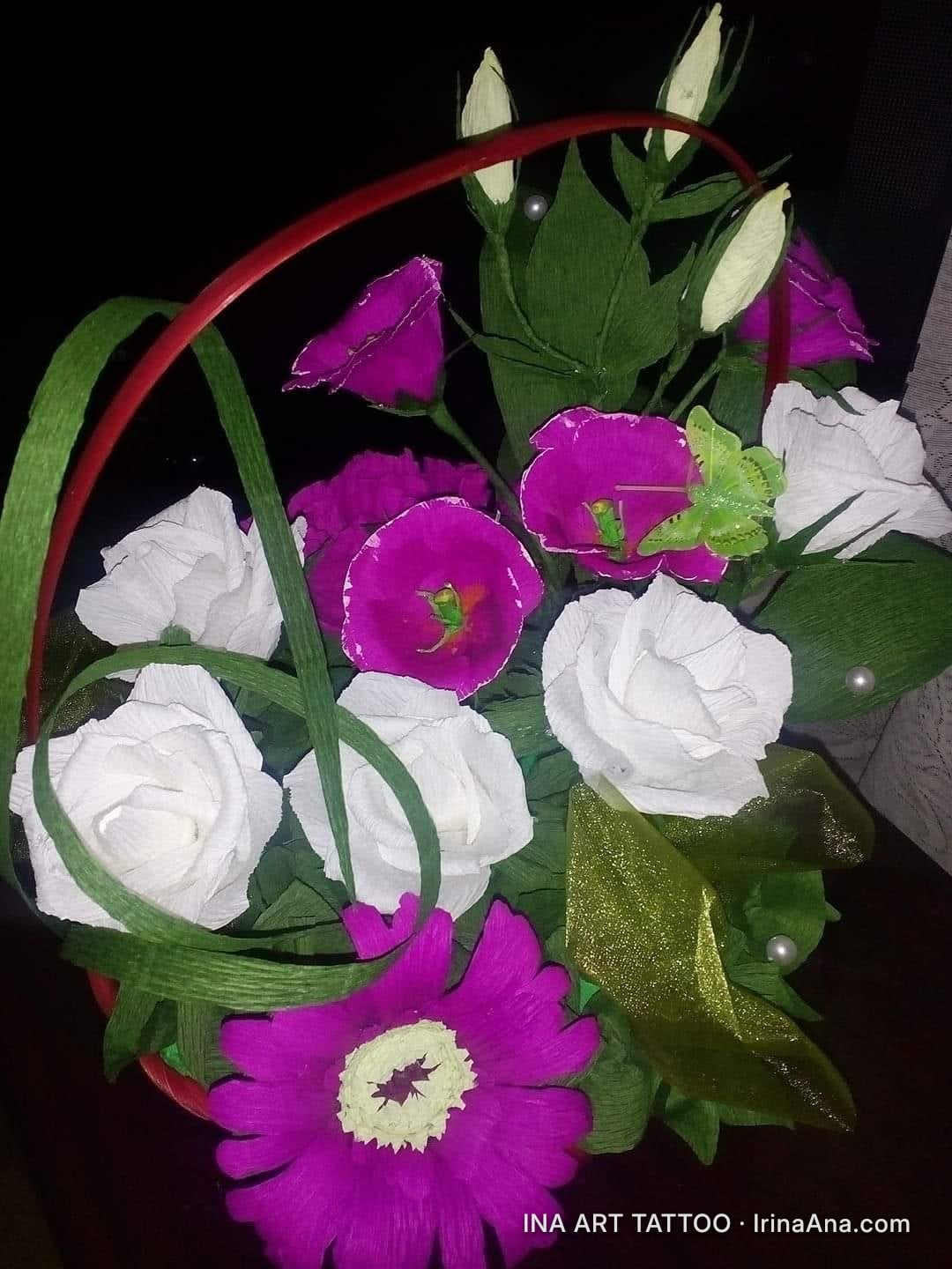 Crepe paper flower arrangement, with white, magenta flowers and buds, in a red basket.