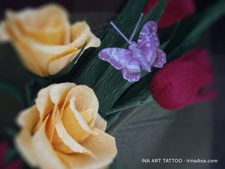 Crepe paper floral arrangement with two yellow flowers, one red flower, and a purple glitter butterfly.