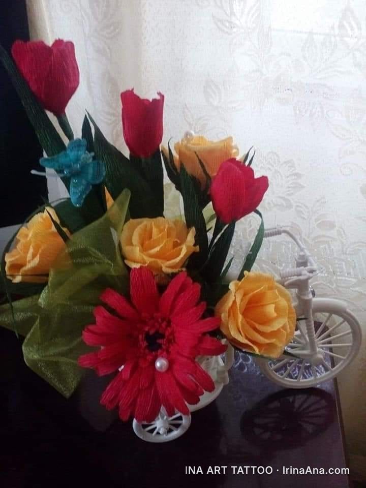 Crepe paper flower arrangement with yellow roses, red tulips, and a red gerbera with a pearl, in a white pot.