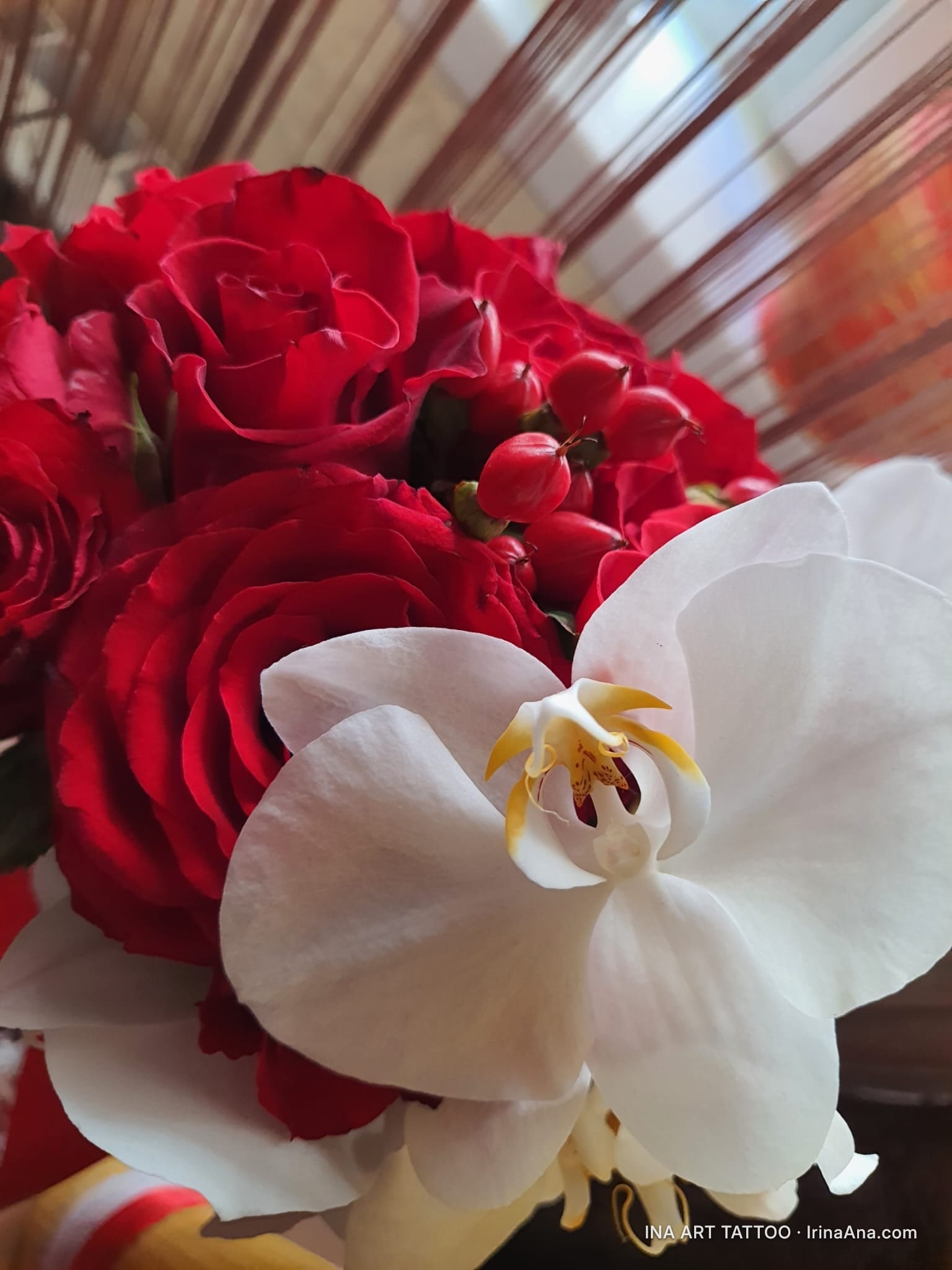 Floral bouquet with red roses, red berries, and a white orchid with delicate petals and a yellow center.