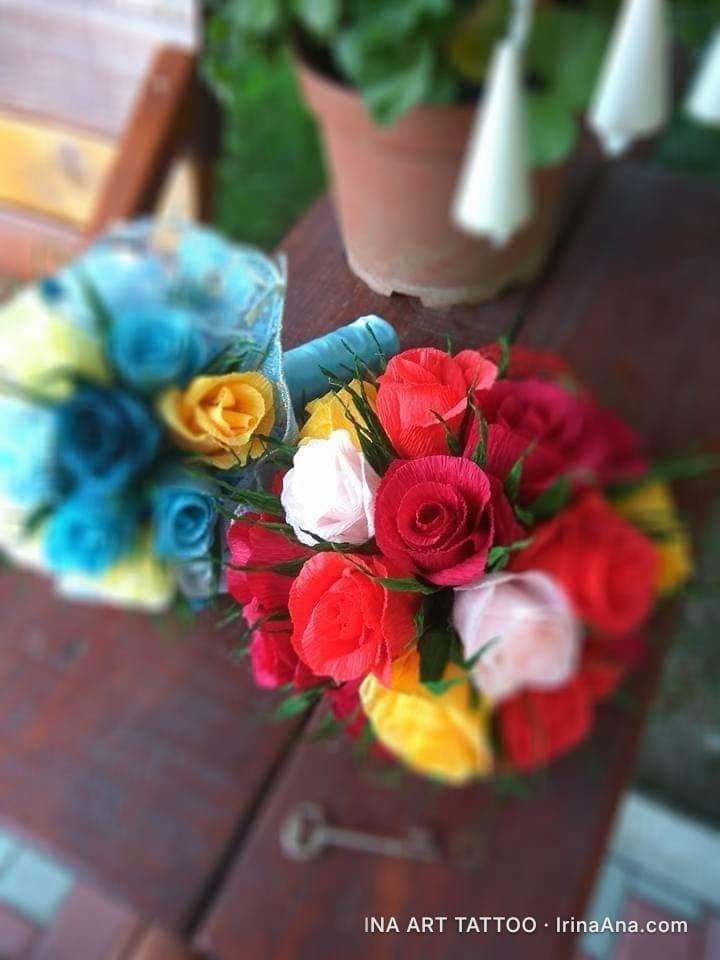 Two bouquets of crepe paper flowers, one red-yellow-white and one blue-yellow, on a wooden table.