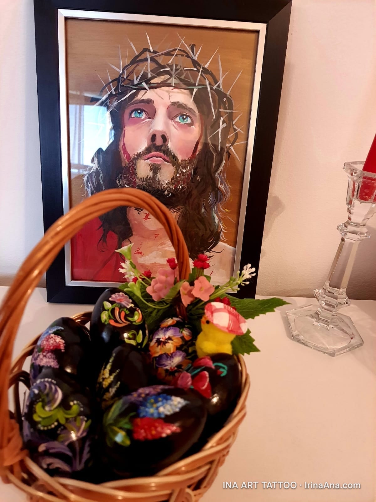 A wicker basket filled with black Easter eggs, hand-painted with colorful floral motifs, alongside artificial flowers.