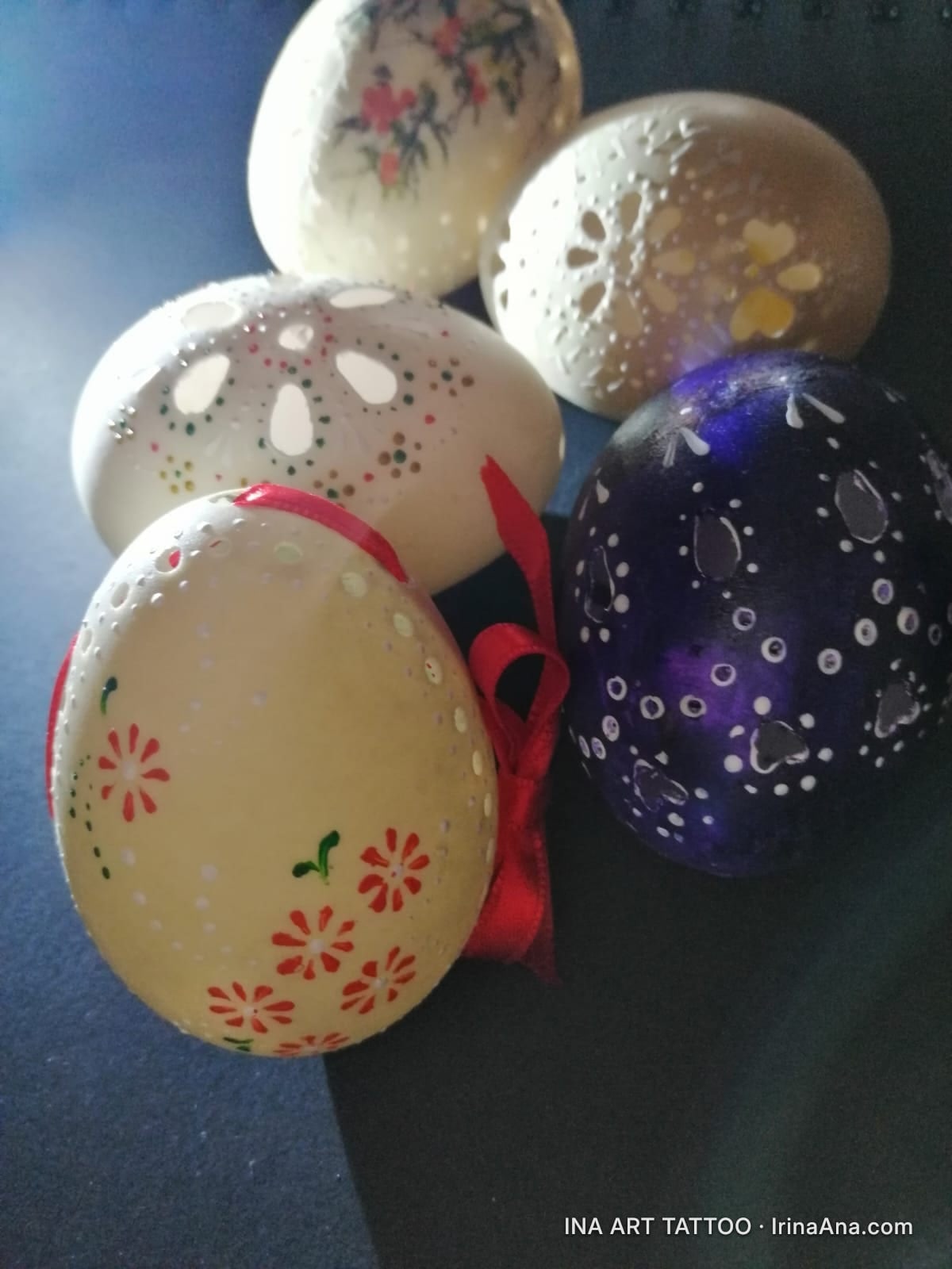 Five decorated Easter eggs, hand-carved and painted with floral and geometric motifs, on a dark blue background.