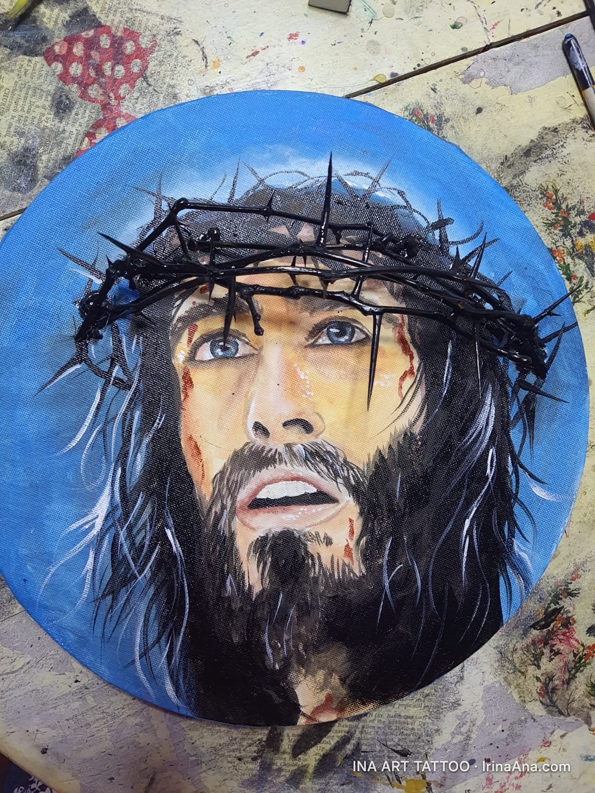 Portrait of a bearded man with long hair, wearing a crown of thorns, against a blue background. His expression is one of suf…