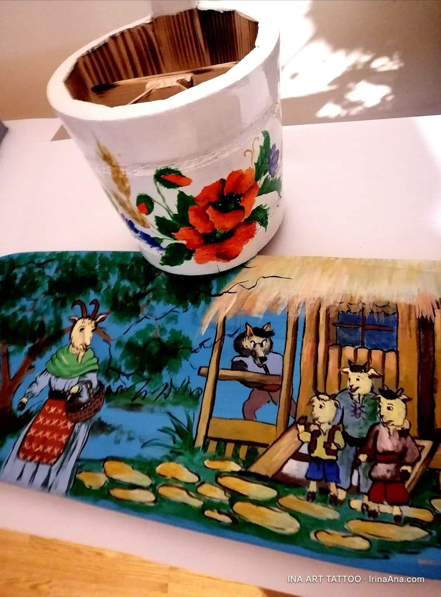 A wooden bucket painted with poppies and a board depicting a scene from The Goat with Three Kids: the goat, the wolf, and th…