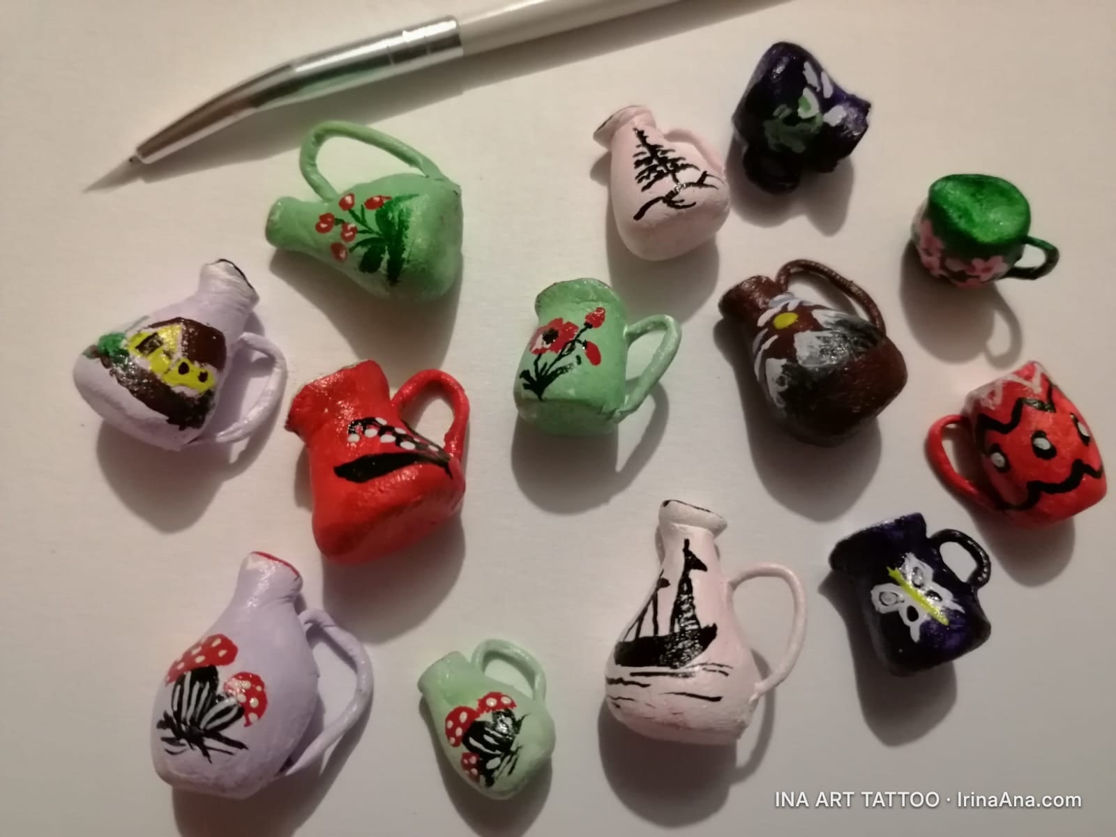 Twelve hand-painted ceramic miniatures, depicting pitchers, mugs, and cups, next to a painting brush.