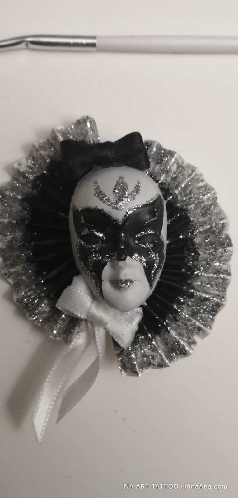Decorative Mărțișor with a white and black mask, with silver glitter, on a pleated background, with a black and a white bow.