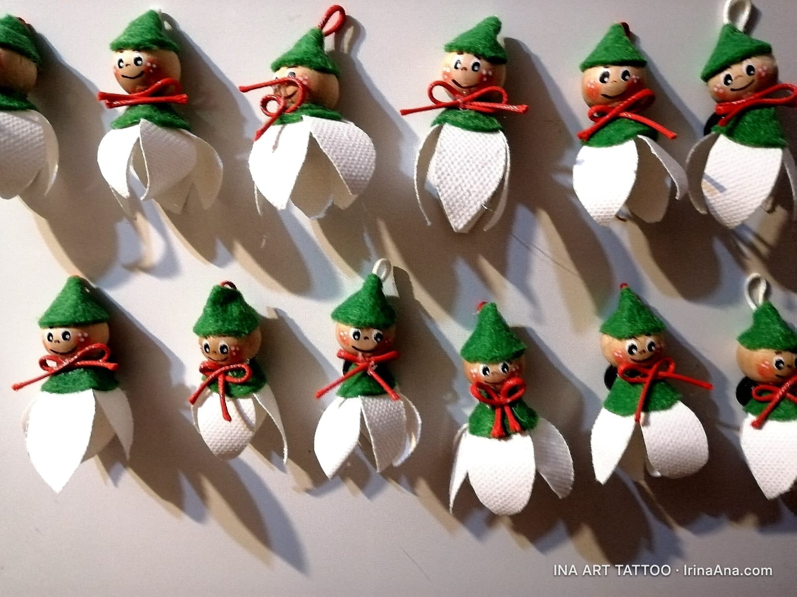 Two rows of handmade martisor figurines shaped like snowdrops with smiling faces and green hats.