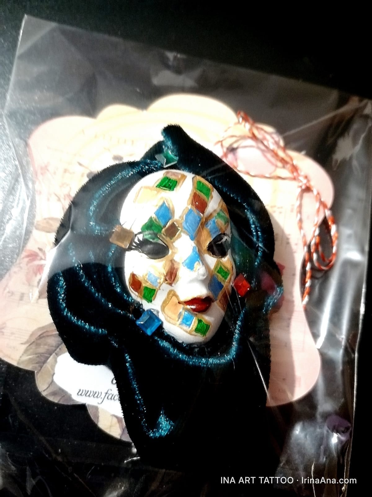 Martisor brooch shaped like a white Venetian mask with colorful diamonds, packaged in clear plastic.