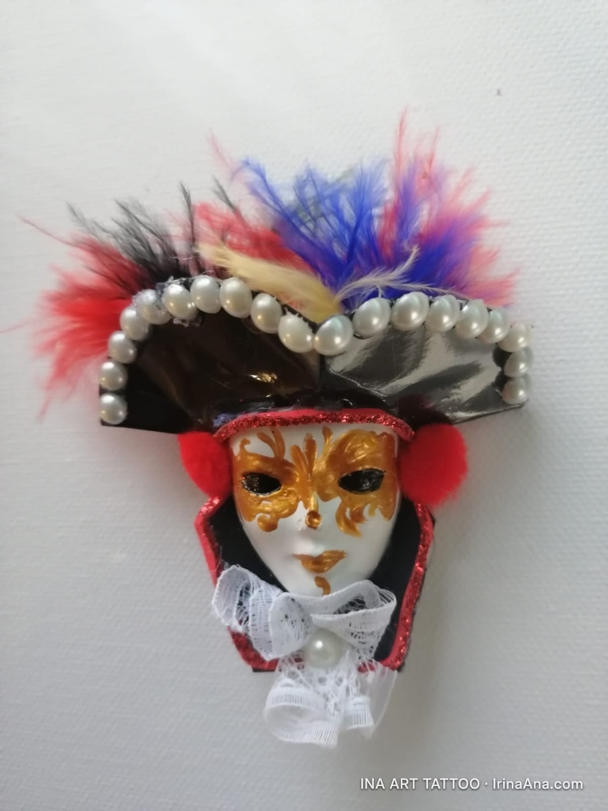 Mărțișor: white Venetian mask with gold decorations, black hat with red, blue, yellow feathers and white pearls.