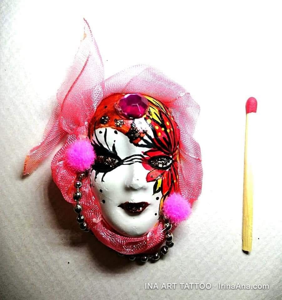 Mărțișor shaped like a Venetian mask, with black, red, and gold makeup, decorated with pink tulle, pom-poms, and a fuchsia s…