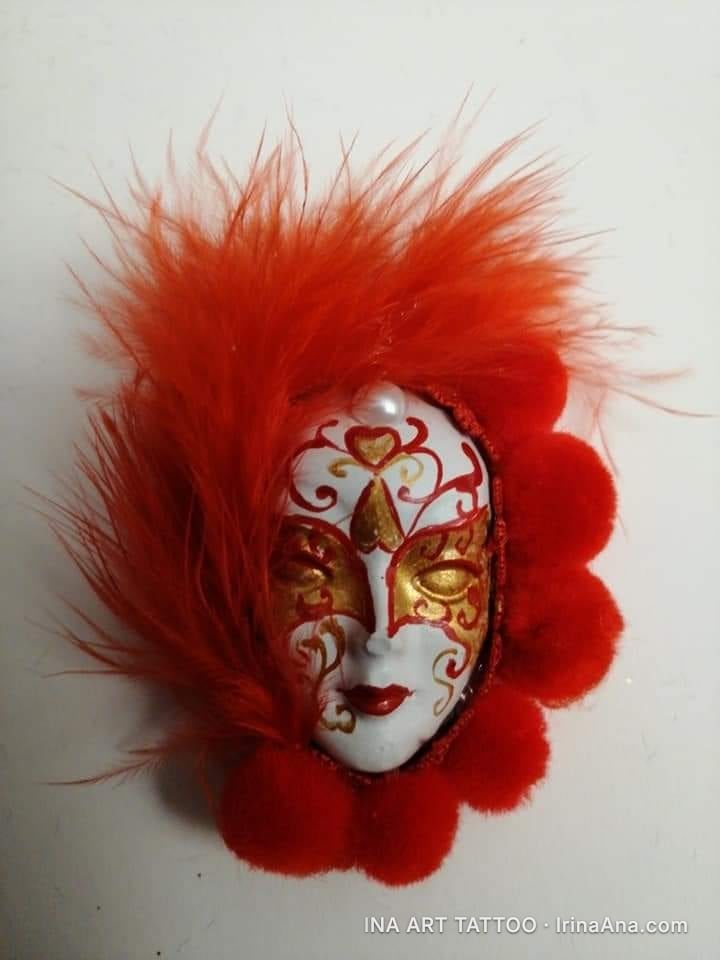 Mărțișor: white Venetian mask with gold and red decorations, surrounded by red feathers and fluffy pom-poms.