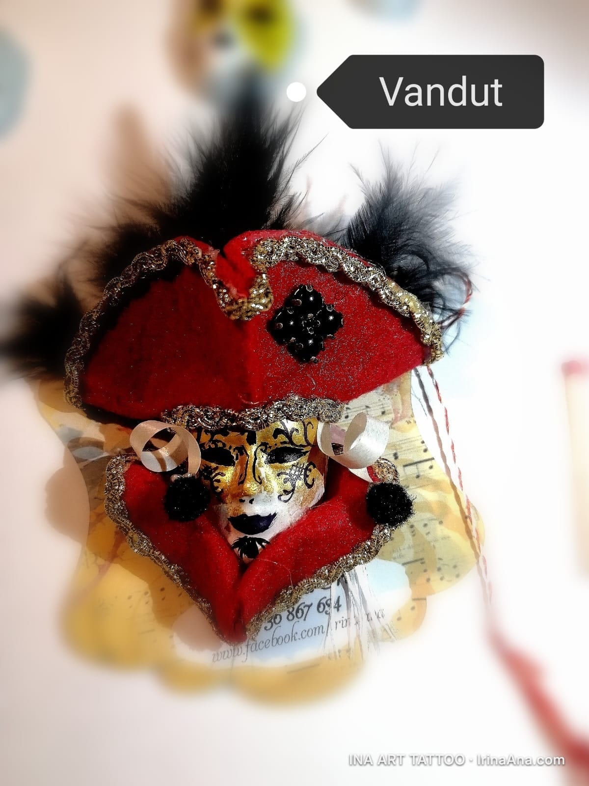 Mărțișor: white and gold Venetian mask with a red hat, decorated with black feathers and gold embroidery.