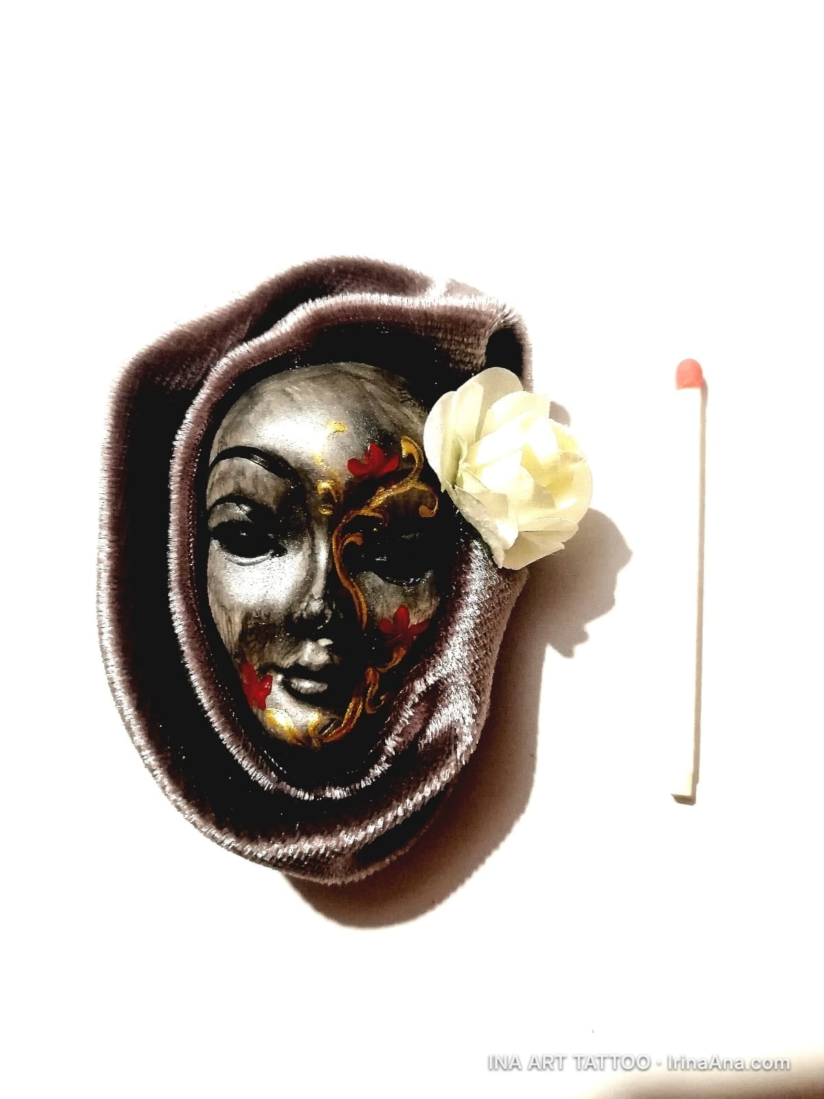 Handmade brooch with a silver Venetian mask, partly gold and red, framed in brown velvet with a white flower.