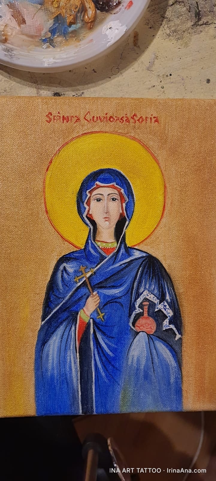 Icon painting of Saint Sophia, dressed in blue, holding a cross and a vessel, on a golden background.