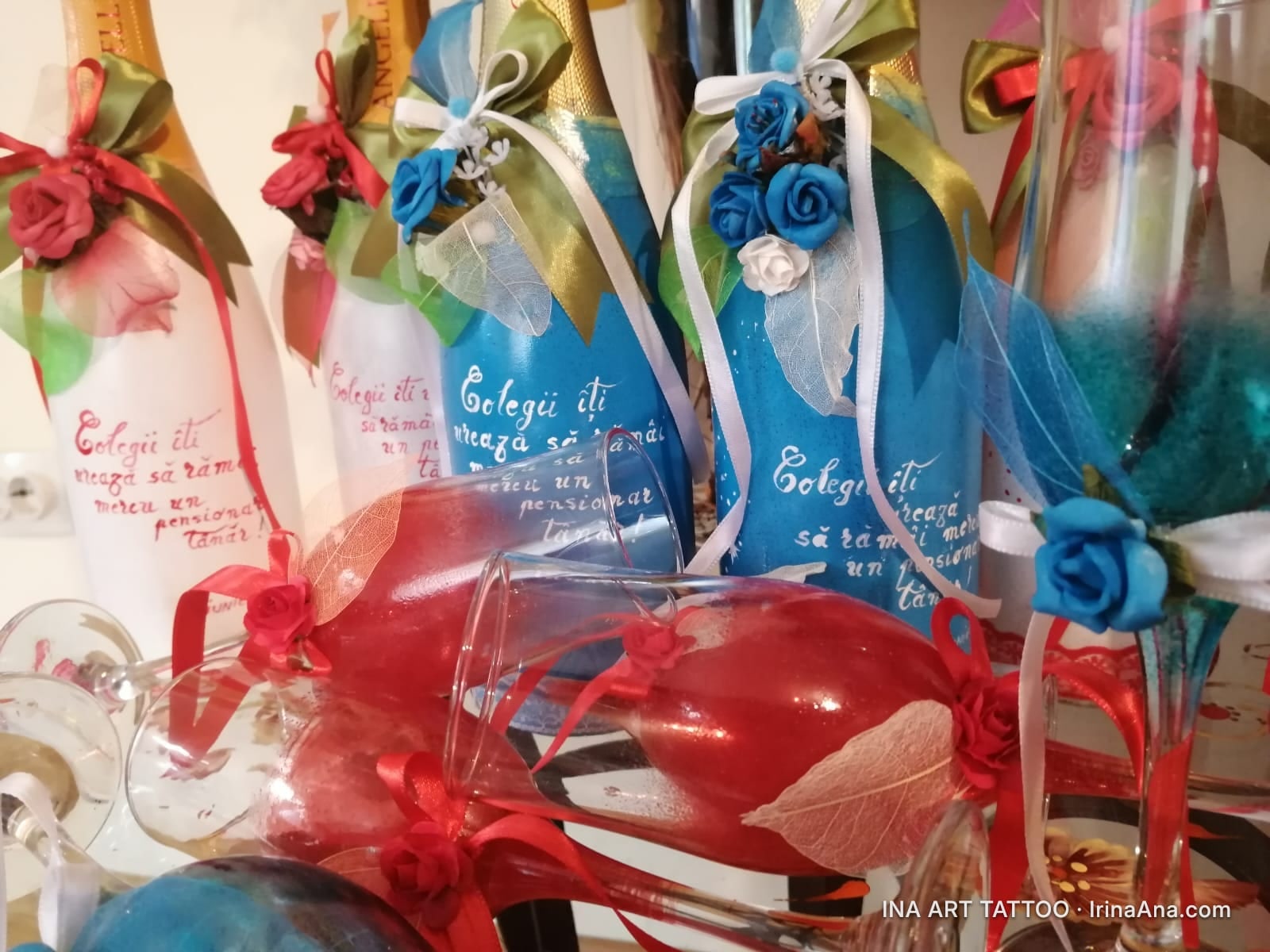 Trei sticle de șampanie decorate cu panglici și flori, și două pahare de vin roșii, decorate cu panglici roșii.