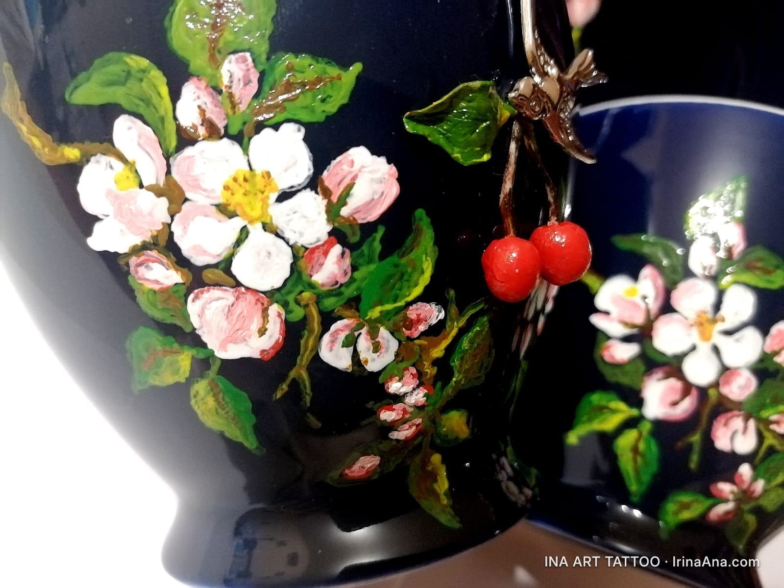 Detalii de pictură manuală cu flori albe și roz de cireș, frunze verzi și cireșe roșii pe ceramică albastru închis.