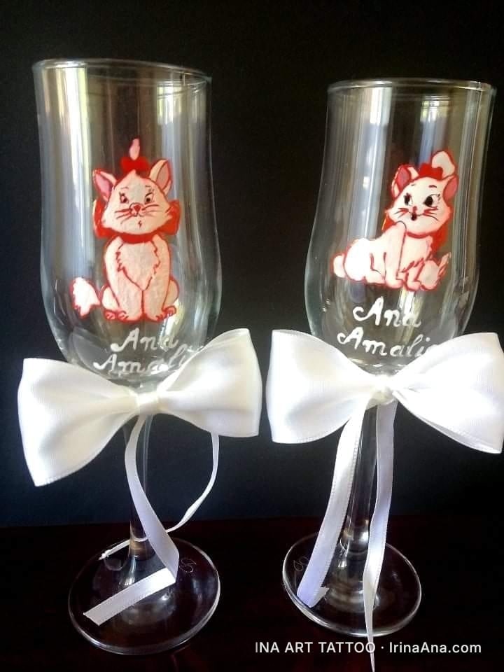 Două pahare de vin decorate cu pisici Marie din desene animate, cu fundițe albe din satin și nume scrise.