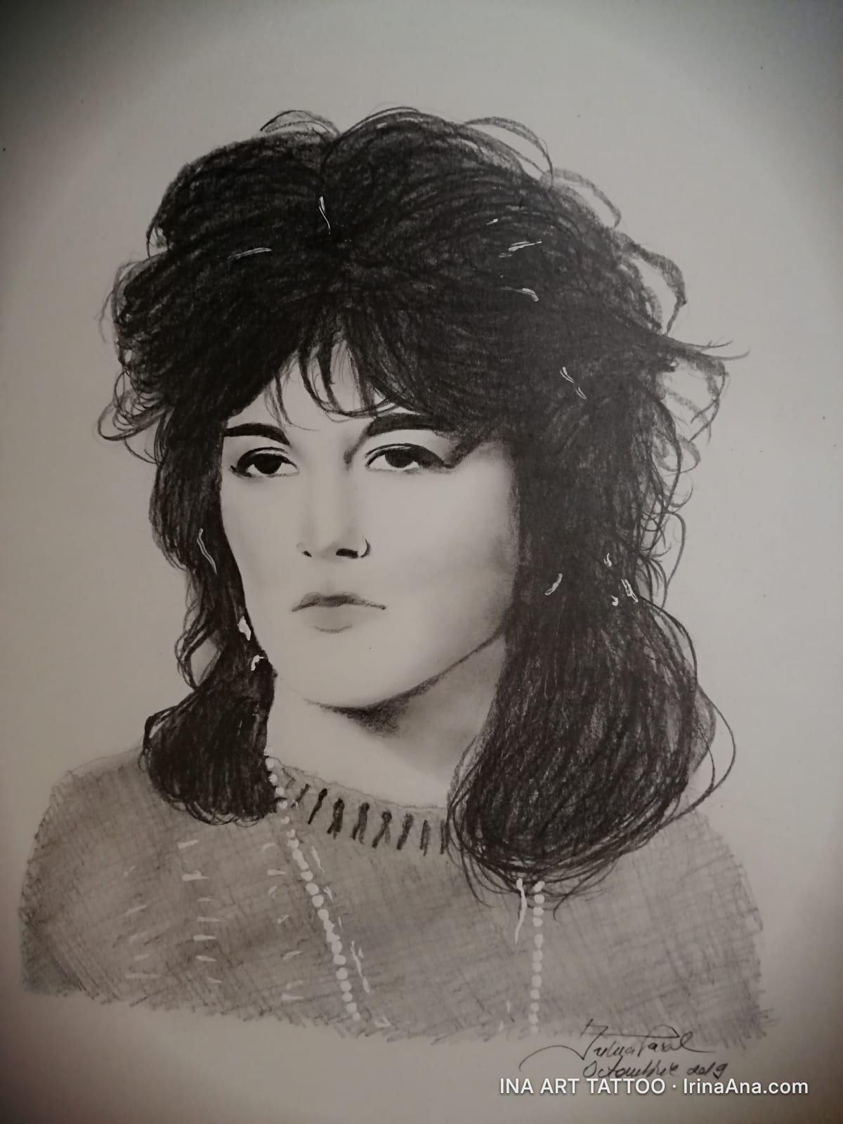 Portret creion al unei femei cu păr voluminos, întunecat, și o expresie serioasă. Poartă un colier de perle și o bluză trico…